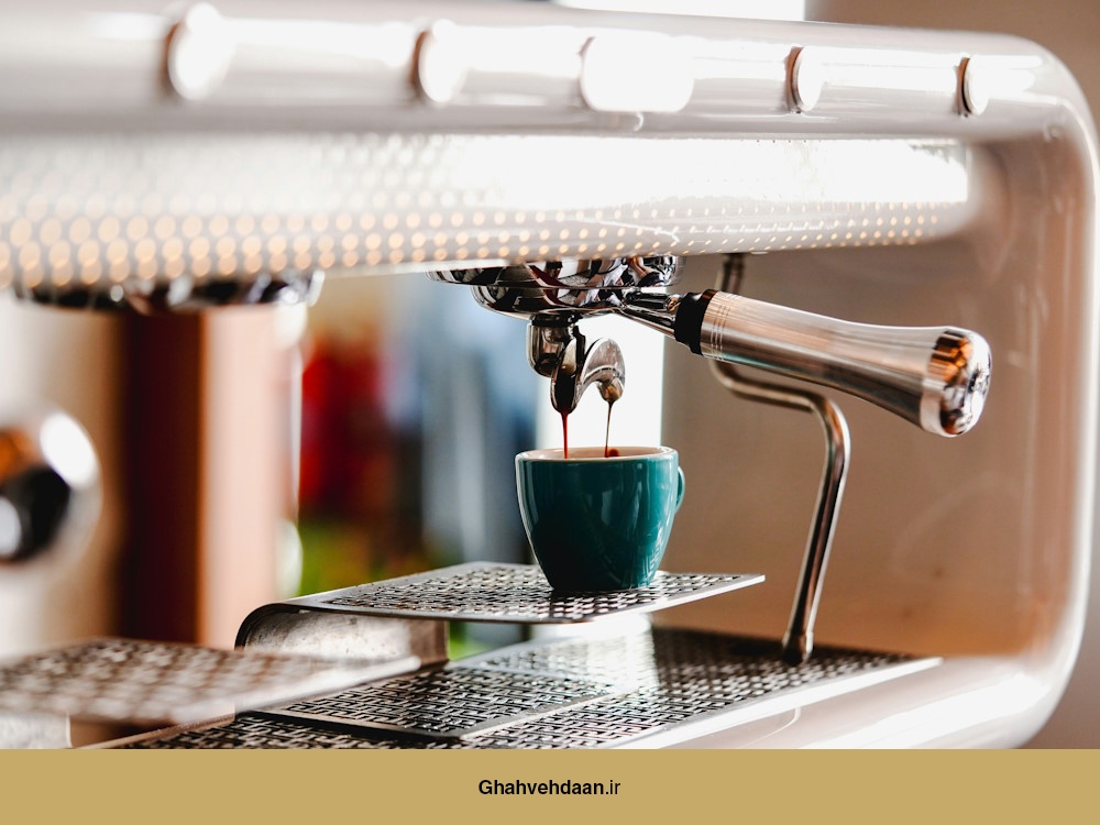 یک شات اسپرسو که از یک دستگاه اسپرسو مدرن با طراحی سفید و براق در حال عصارهگیری است و درون یک فنجان سرامیکی آبی ریخته میشود.